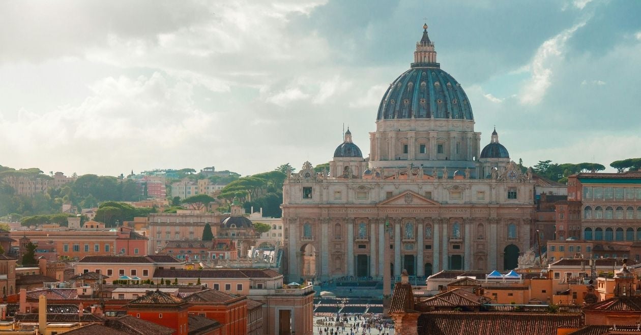 A fachada da Basílica é ampla e feita de pedra clara, com colunas coríntias que sustentam um frontão triangular.